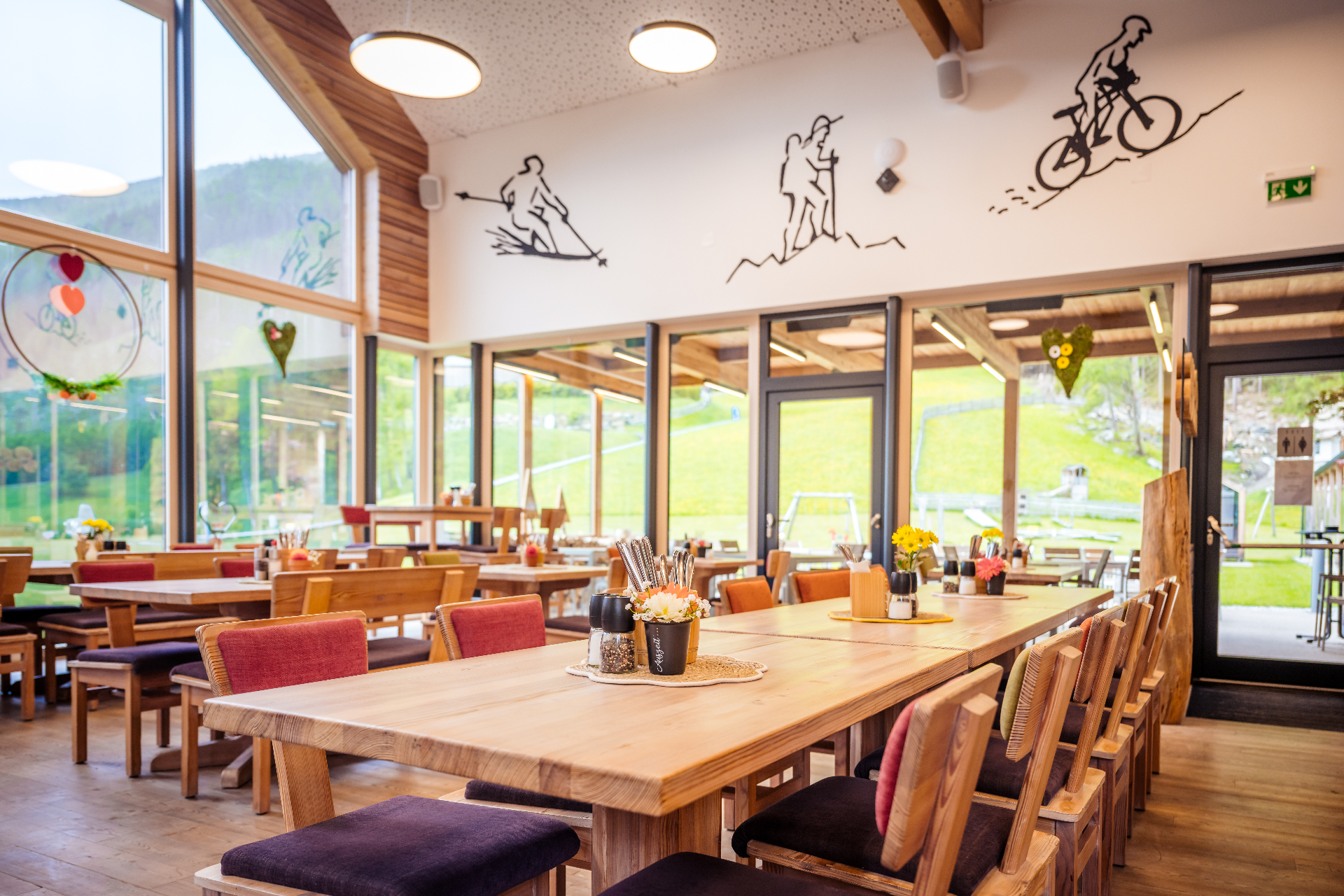 Heller Restaurant-Innenraum mit langen Holztischen und Blick auf die Almwiese